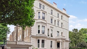 Un edificio de varios pisos con un estilo arquitectónico clásico, que presenta una entrada destacada con columnas, ventanas amplias y un balcón en el piso superior.