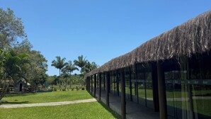 A pathway leading to a building with a thatched roof, surrounded by palm trees and a clear blue sky. - Pousada Village dos Corais  (Matinhos)
