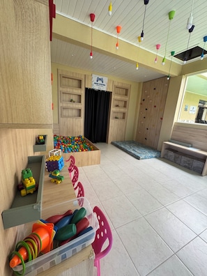 Zona infantil con pared de escalar, luces colgantes de colores y diversos juguetes.