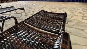A covered outdoor seating area with wicker chairs, a tiled floor, and hanging pendant lights. - Pousada Village dos Corais  (Matinhos)