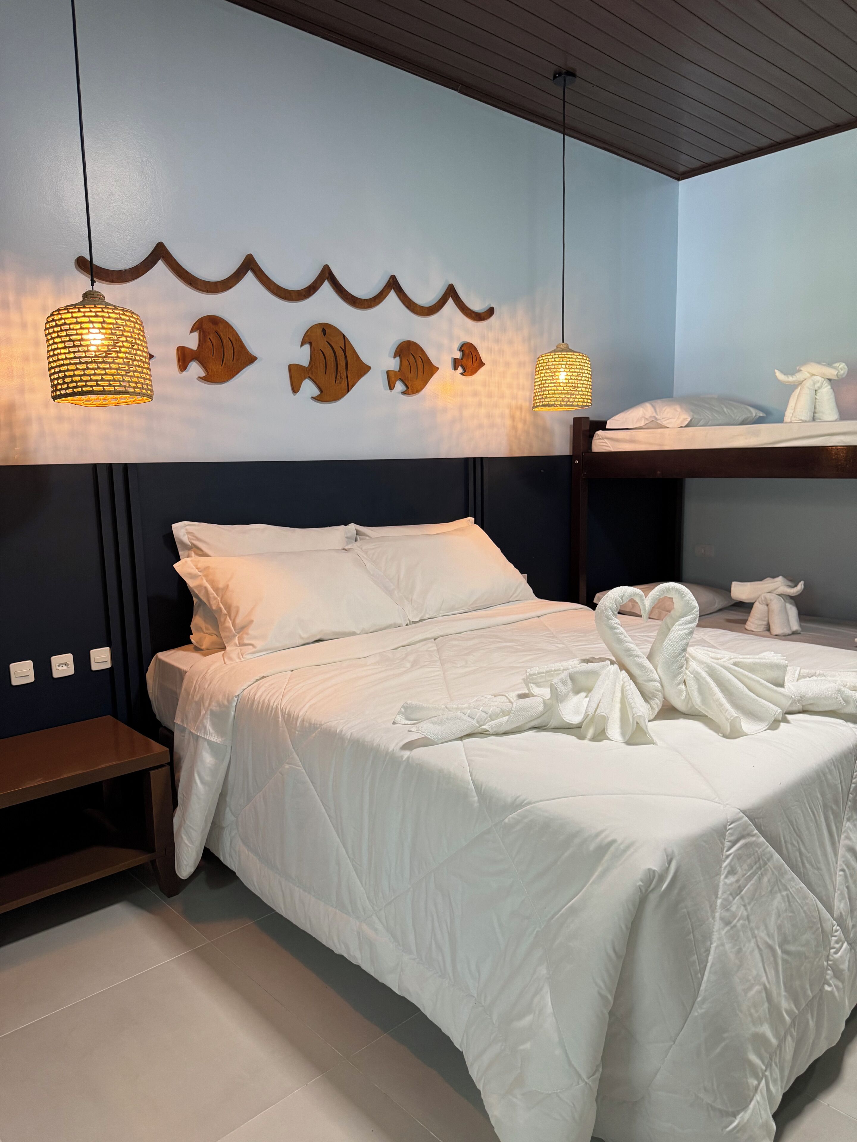 A hotel room with a bed, a nightstand, a wall-mounted shelf with towels, and decorative wall art.