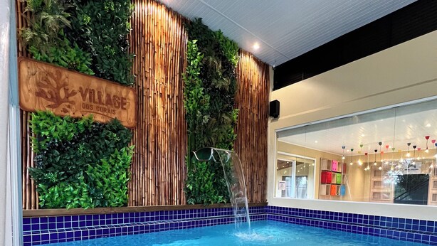 An indoor swimming pool with a wooden wall and a sign that reads 'VILLAGE DUS CURAIS.' - Pousada Village dos Corais  (Matinhos)