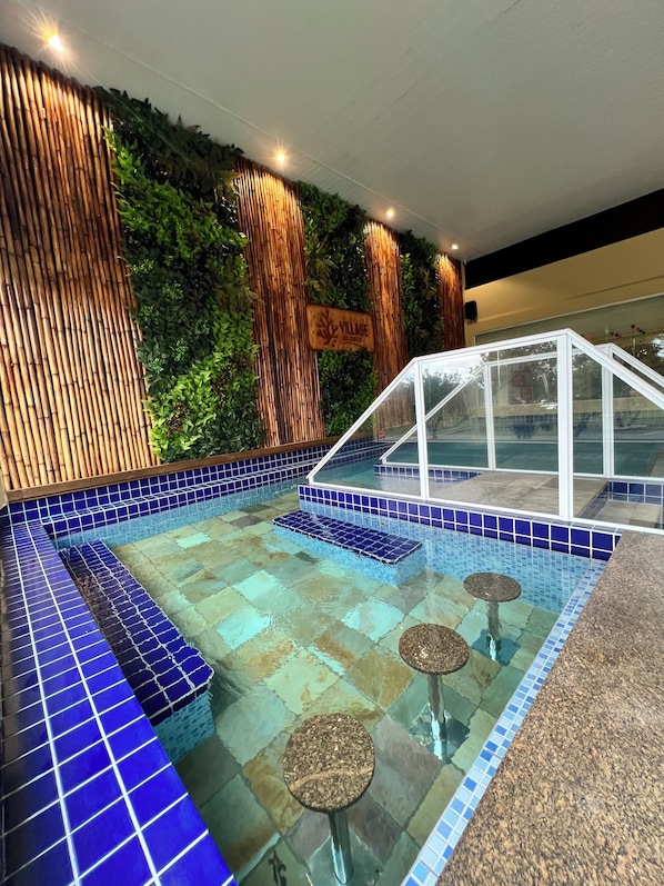 Una piscina interior con azulejos azules, una pared de madera con listones verticales y un cartel que dice 'VILLAGE'.
