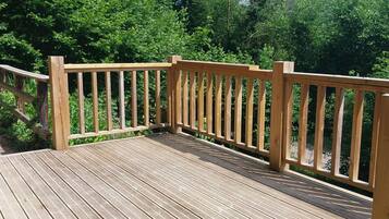 A wooden deck with railings, surrounded by lush greenery.