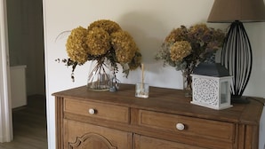 Un meuble en bois avec des tiroirs, une lampe et deux compositions florales sur le dessus.