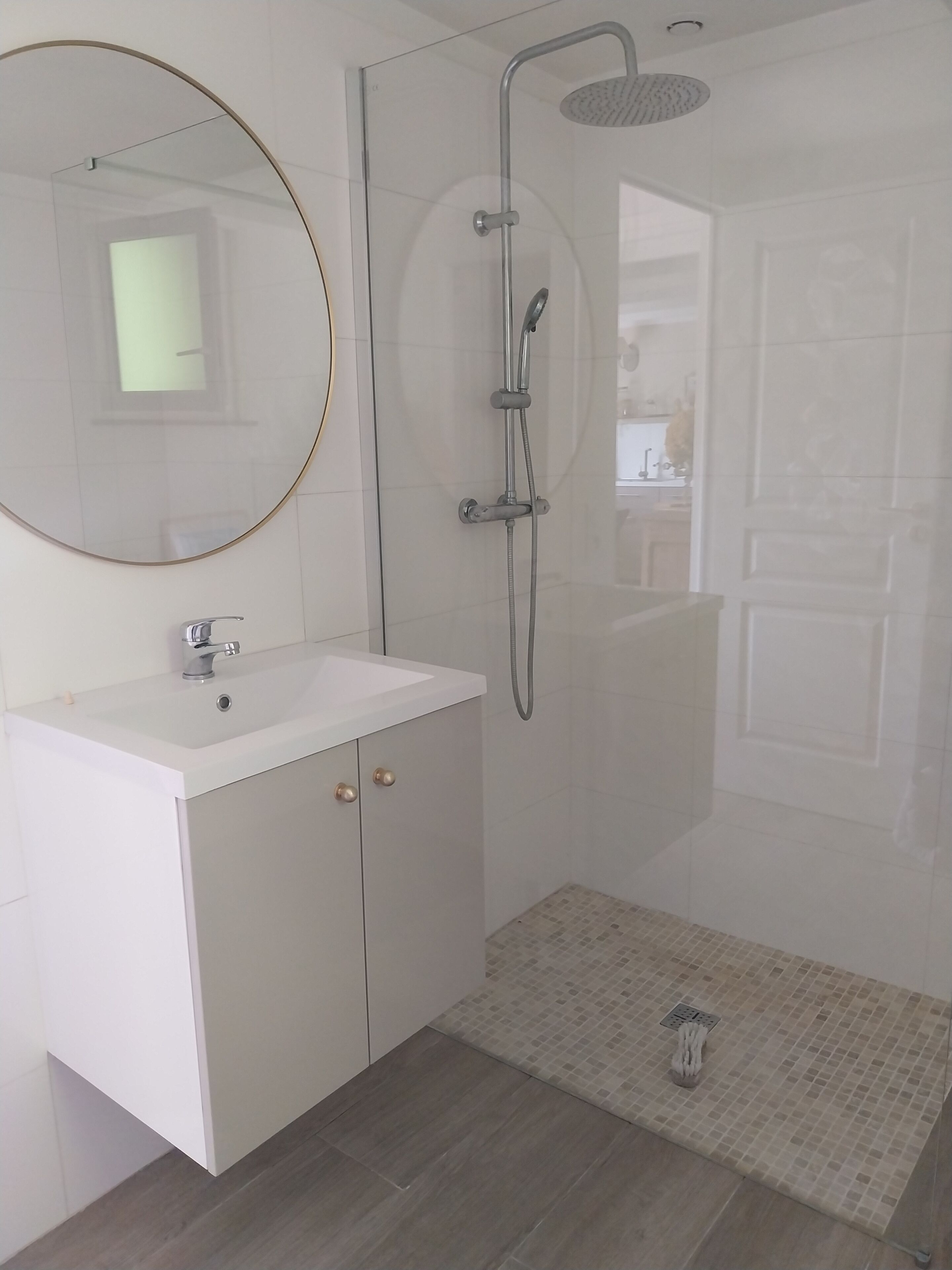 A bathroom with a white sink, a round mirror, a shower with a handheld showerhead, and a tiled floor.