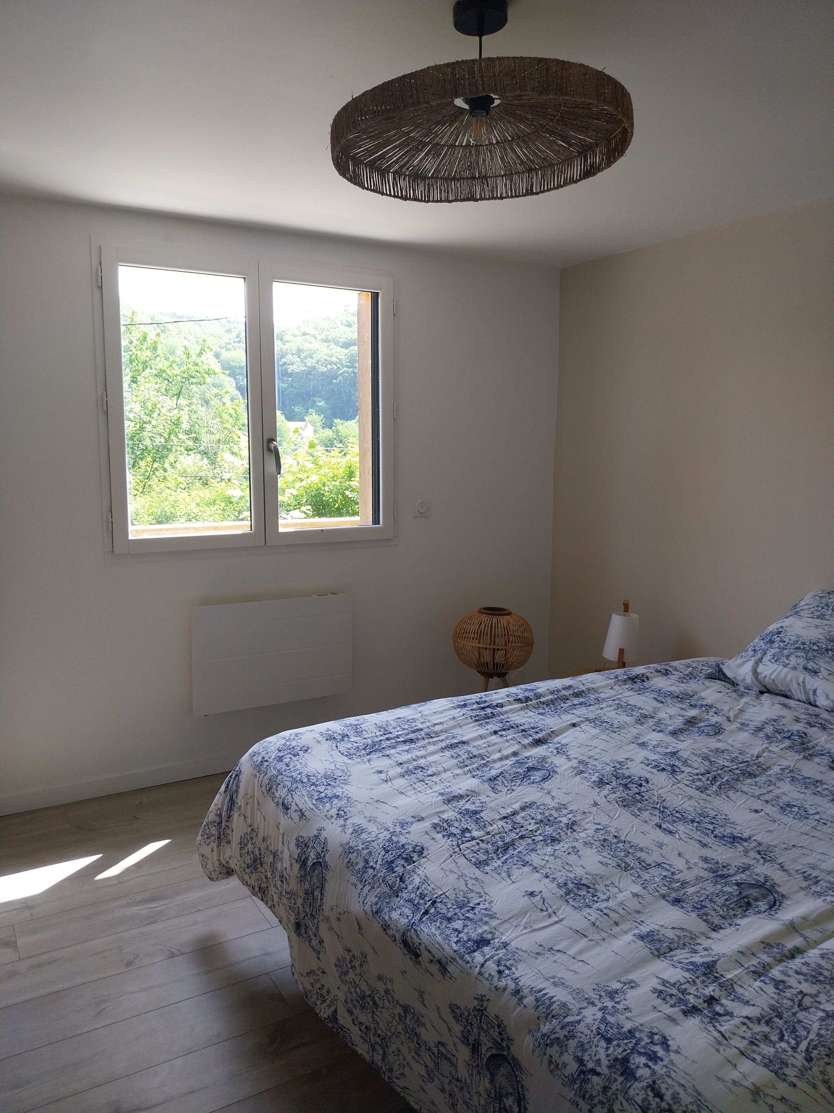 A bedroom with a bed, a window with a view, a radiator, and a hanging light fixture.