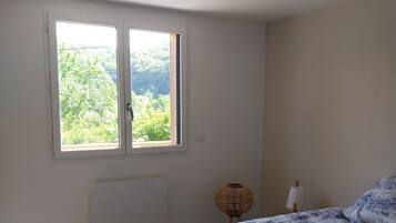 A bedroom with a bed, a window with a view, a radiator, and a hanging light fixture.