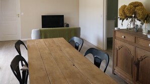 Un coin repas avec une table en bois, des chaises noires, un téléviseur et une plante décorative.