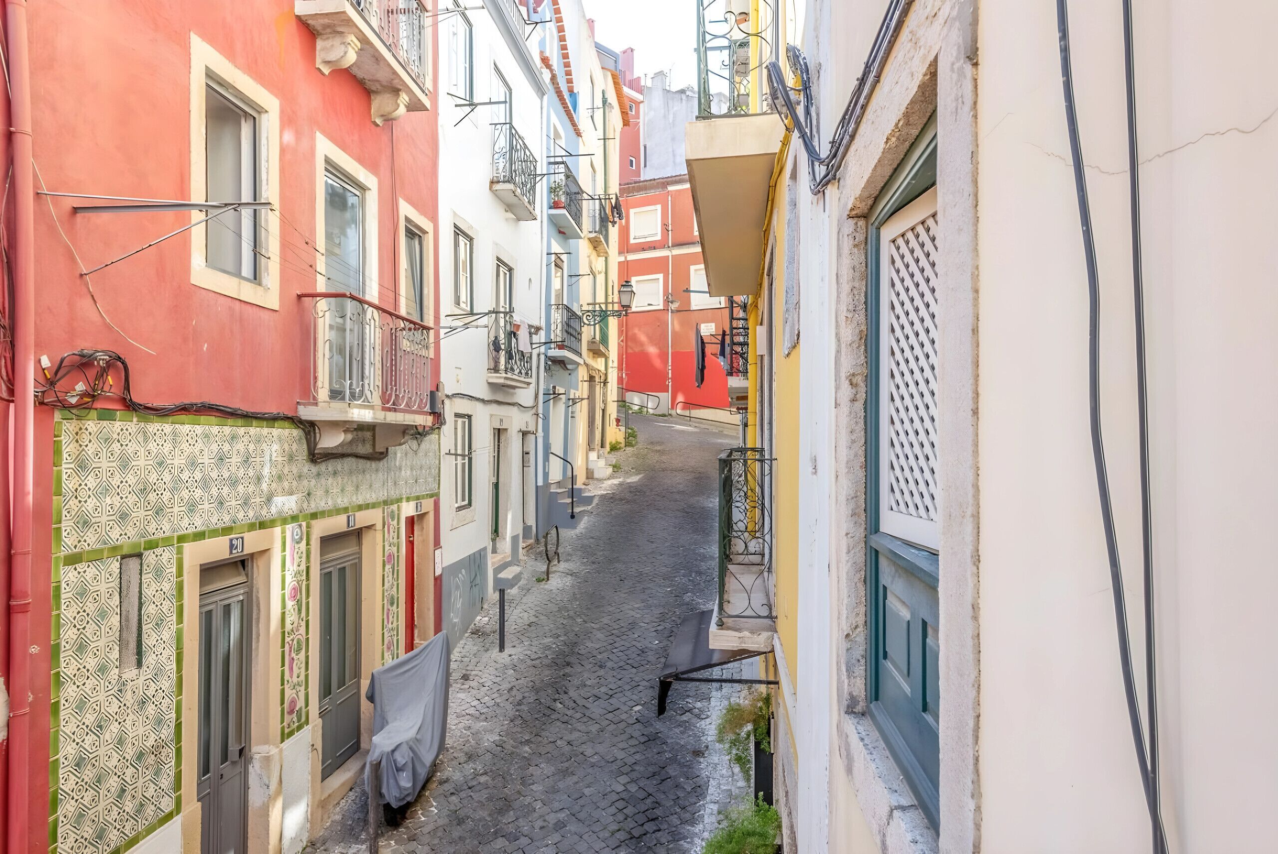 Una stretta strada acciottolata, fiancheggiata da edifici colorati con balconi e persiane.