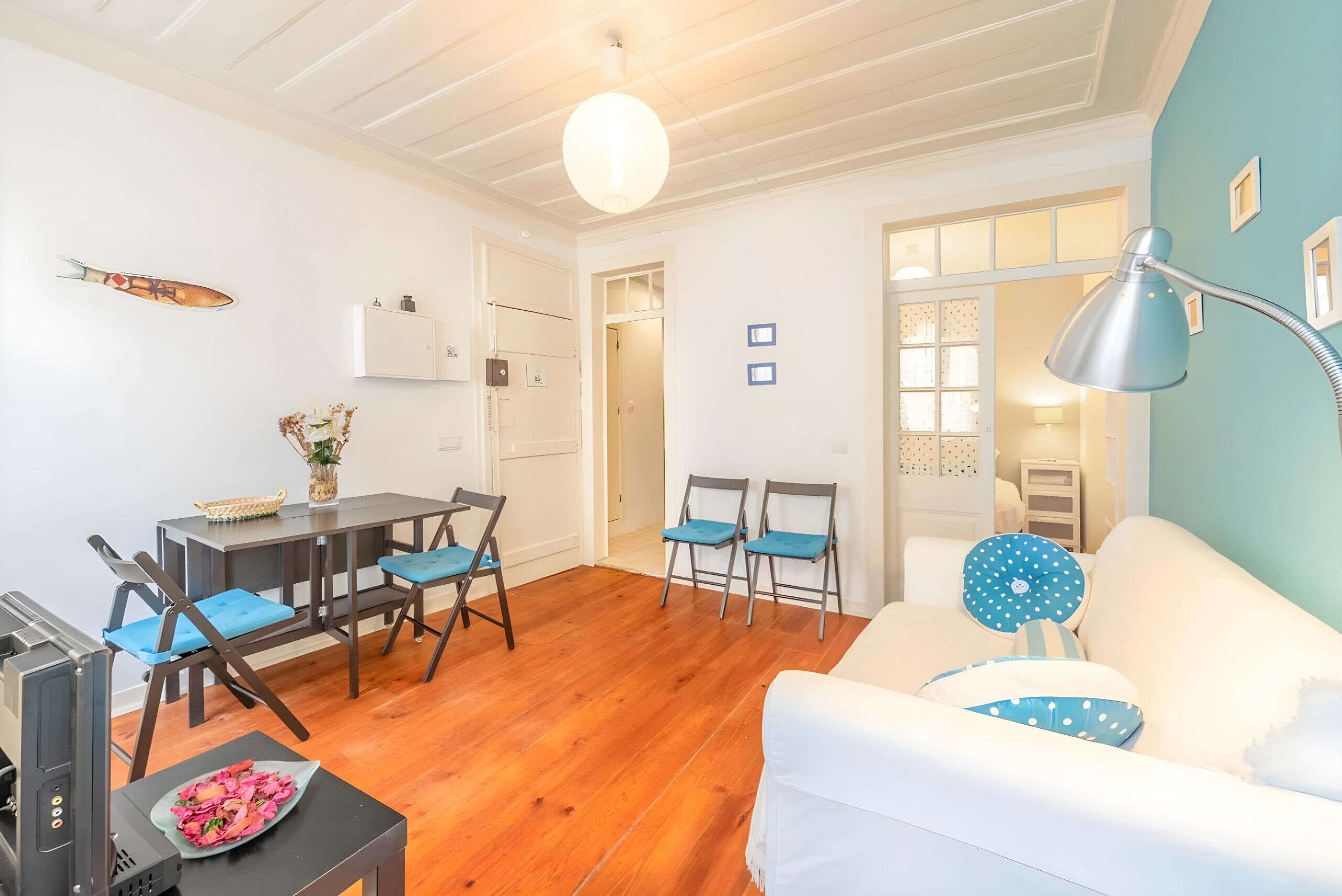 Un salon avec un canapé blanc, des fauteuils bleus, une table à manger et un coin cuisine doté de placards.