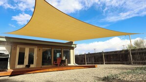Una casa con patio cubierto, jardín cercado y cielo despejado.