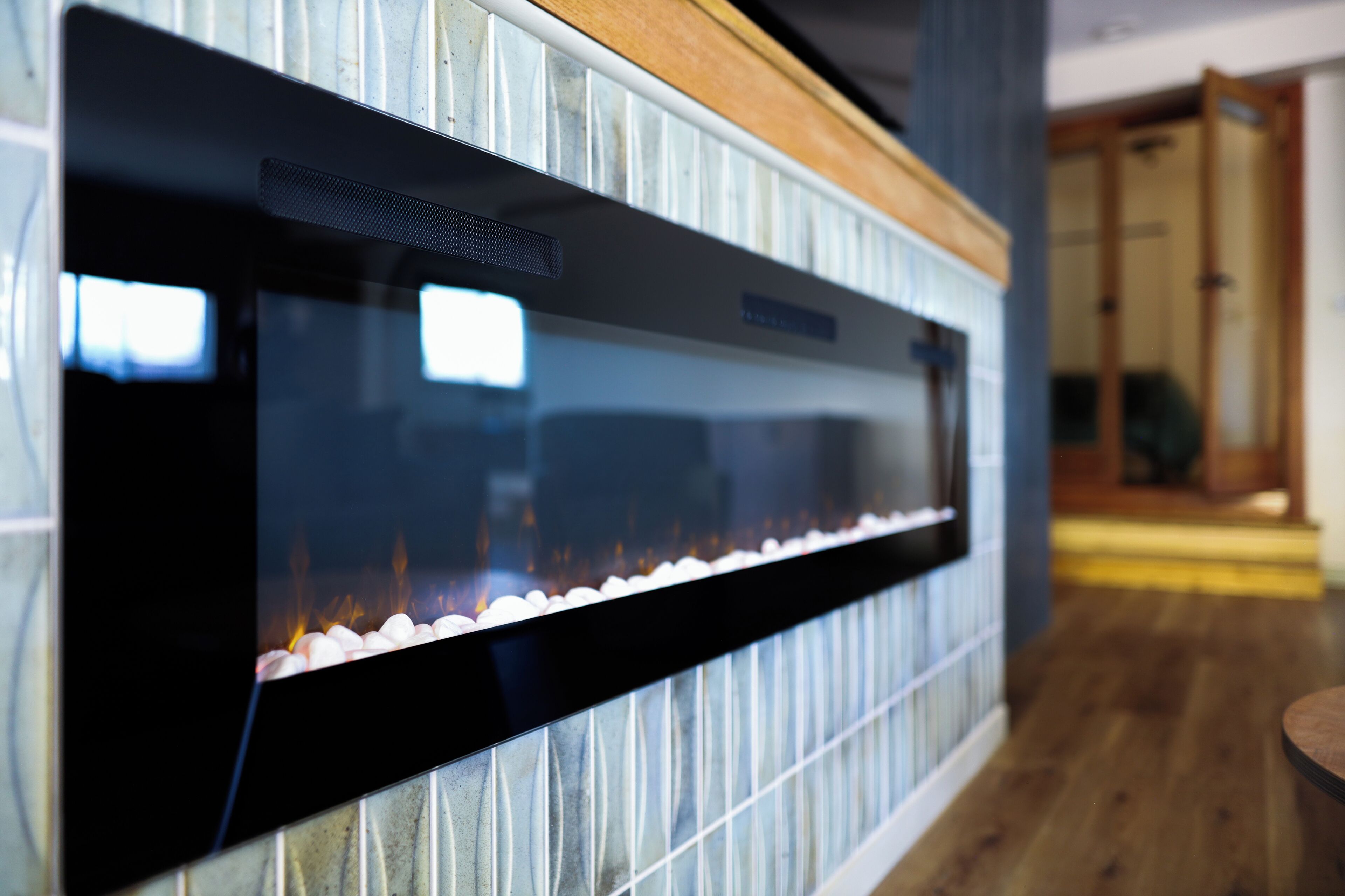 Ein moderner Kamin mit Glasfront, hölzernem Sims und einer Wand mit Fliesen.