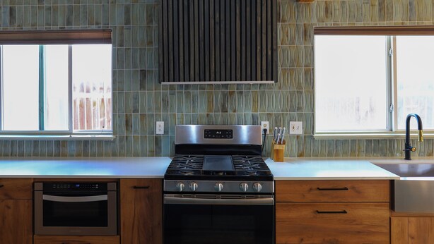 Una cocina moderna con estufa, horno y lavavajillas integrados, ventanas amplias y un salpicadero decorativo.