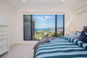 Ein Schlafzimmer mit einer großen Schiebeglasdoor, einem Bett mit gestreifter Bettwäsche, einem Schminktisch und einem Nachttisch mit Lampe.