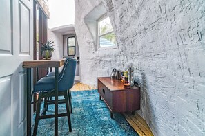 A room with a rustic white brick wall, a wooden bench, a blue patterned rug, and a small wooden side table with various items.
