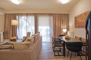 A modern living room with a sofa, dining table, chairs, and a large window with curtains. - Holiday Infinity View (Nea Smirni)