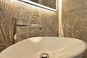 Une salle de bain avec un lavabo blanc, un robinet chromé et un mur orné d’un motif de feuilles.