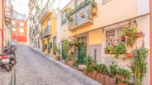 A narrow cobblestone street lined with colorful buildings, some with balconies and potted plants. - Historic Typical 1 By Gt House (Lisbon)