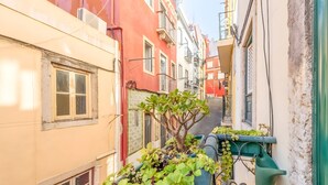 A narrow urban alley with buildings on either side, featuring balconies with plants and a green watering can. - Historic Typical 1 By Gt House (Lisbon)