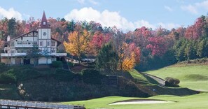 Ein Gebäude mit einem Glockenturm, umgeben von Bäumen in Herbstfarben und einem Golfplatz.