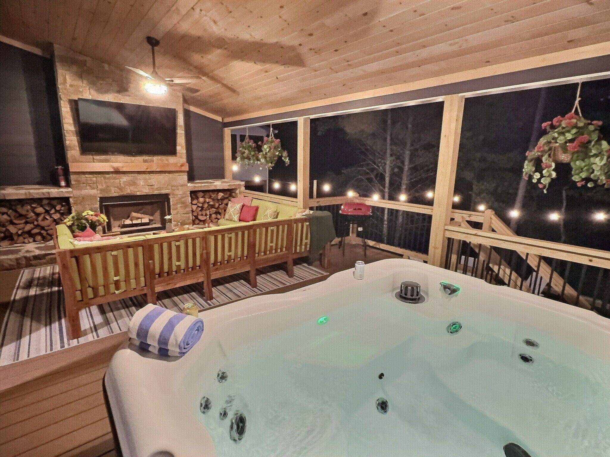 Une terrasse en bois avec un jacuzzi, une cheminée en pierre et un coin salon agrémenté de coussins.