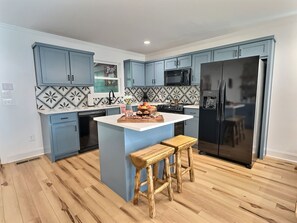 Eine moderne Küche mit blauen Schränken, einer zentralen Kochinsel, Holzbarhocker und einem Edelstahlkühlschrank.