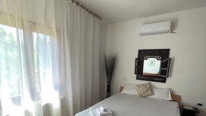 Une chambre à coucher comprenant un lit, des rideaux, un appareil de climatisation, une table de chevet et un miroir fixé au mur.