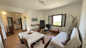 Une pièce comprenant une table à manger, deux chaises, un canapé, un téléviseur, une petite table avec une lampe et une fenêtre donnant sur un beau paysage.