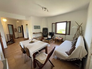 Ein Zimmer mit Esstisch, zwei Stühlen, einer Couch, einem Fernseher, einem kleinen Tisch mit Lampe und einem Fenster mit Blick.