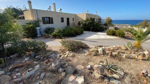 Un bâtiment situé sur la côte, doté d’une allée pavée, entouré de rochers et d’arbustes, et offrant une vue dégagée sur la mer.
