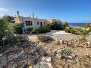 Ein Küstenhaus mit befestigter Auffahrt, umgeben von Felsen und Sträuchern, mit freiem Blick auf das Meer.