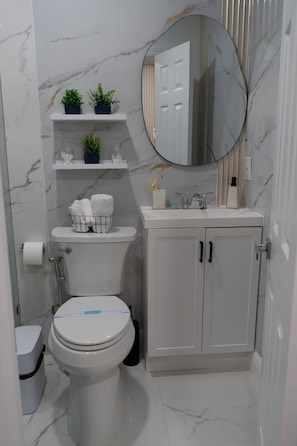 A bathroom with a toilet, sink, mirror, and shelves with plants. -  1-bedroom apartment near The Hard Rock Stadium (Miami Gardens)