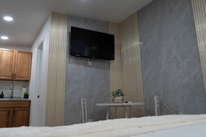 A modern bathroom with a flat-screen TV mounted on the wall, a small table with a plant, and wooden cabinets. -  1-bedroom apartment near The Hard Rock Stadium (Miami Gardens)