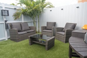 A backyard with a white fence, wicker furniture, a glass coffee table, and a small tree. -  1-bedroom apartment near The Hard Rock Stadium (Miami Gardens)