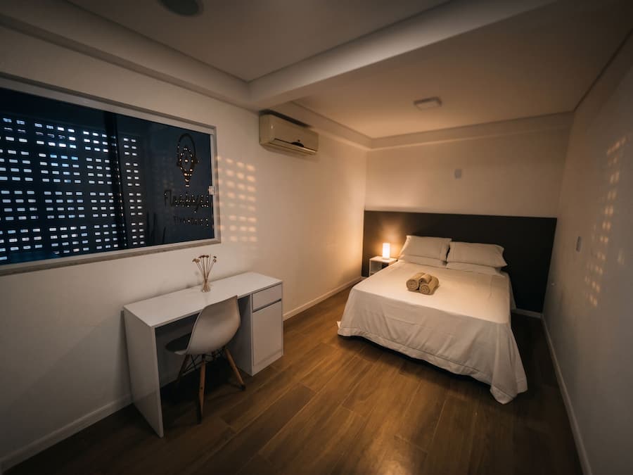 Un dormitorio con cama, mesita de noche, escritorio, silla y ventana con persianas.
