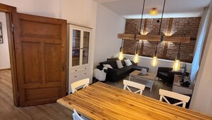 Ein Essbereich mit Holztisch und weißen Stühlen, einer Ziegelwand und hängenden Lampen.