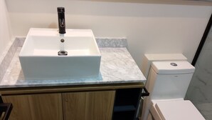 A bathroom with a white sink, a toilet, and wooden cabinets. - LUUM 202 (Guadalajara)