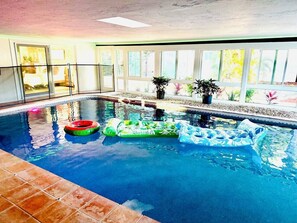 Ein Innenpool mit großen Glaswänden, gefliestem Boden und mehreren aufblasbaren Spielzeugen.