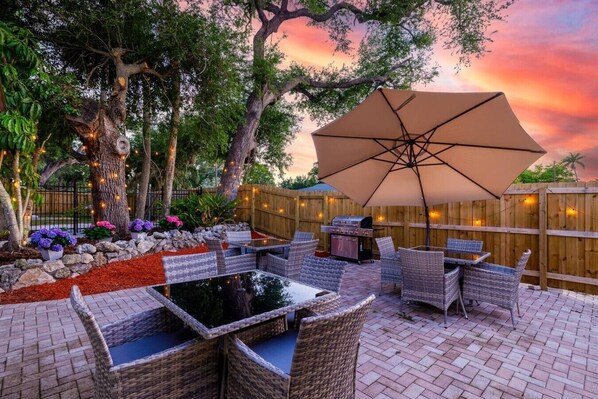 Eine Terrasse im Freien mit Korbmöbeln, einem Grill und einem großen Sonnenschirm.