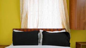 A bed with black and white pillows, a wooden headboard, and a window with a sheer curtain.