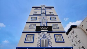A multi-story building with a central vertical design element and a sign indicating it is a serviced apartment. - Classic Airport Stay (Nelamangala)