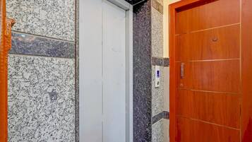 A hallway with a marble wall, a white elevator door, and a wooden door.