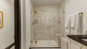 Une salle de bain moderne avec une douche à parois de verre, un sol en marbre et des accessoires dorés.
