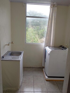 Ein kleines, sauberes Badezimmer mit Fenster, Waschbecken und Waschmaschine.