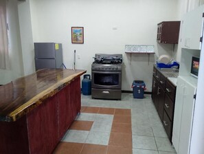 Eine Küche mit Gasherd, Backofen, Kühlschrank und einer Holzausziehtischplatte.