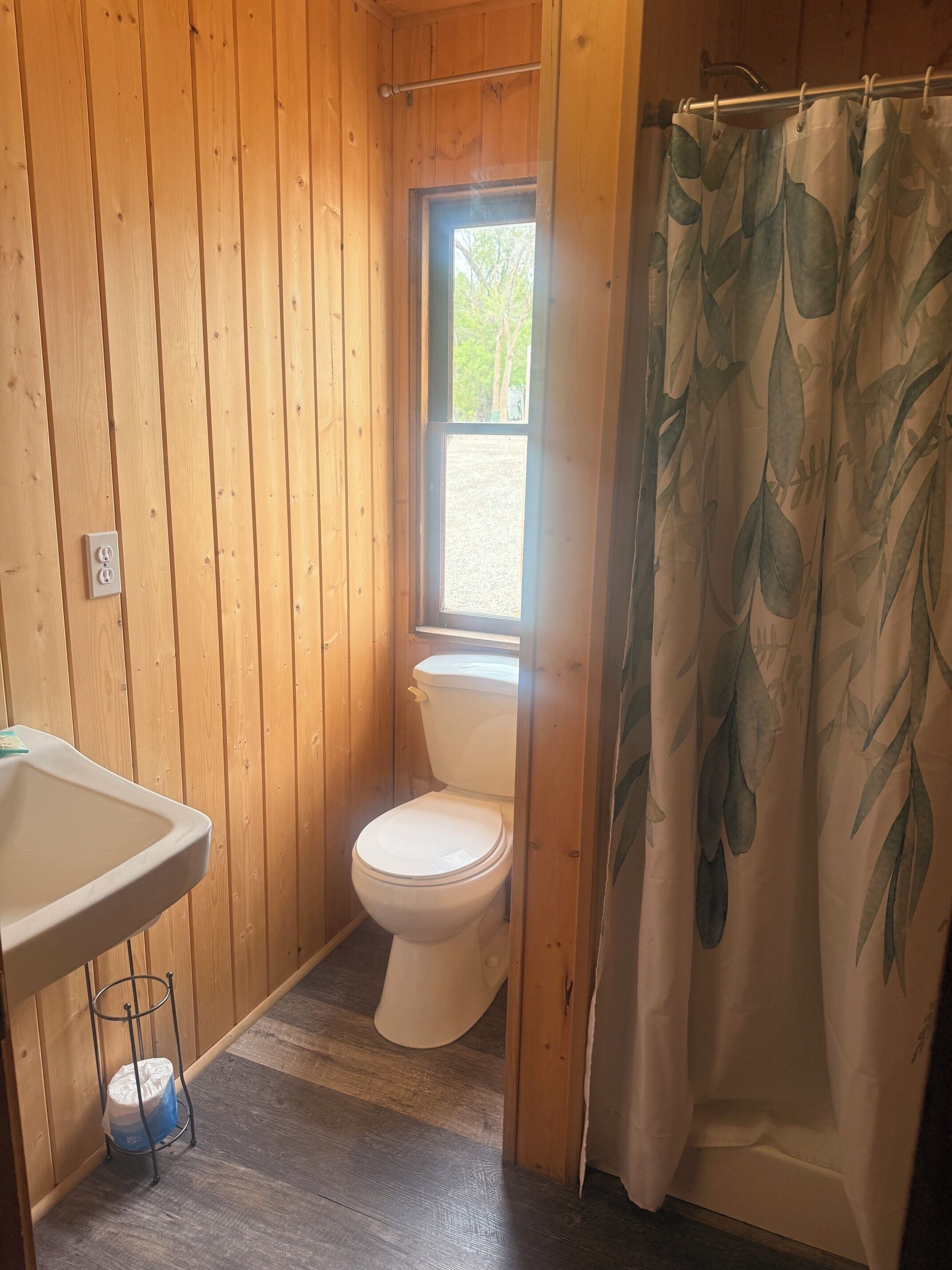 Un baño con paneles de madera, un inodoro, una ventana y una cortina de ducha.