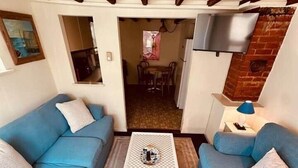 A living room with two blue sofas, a white coffee table, and a TV mounted on a brick wall. - Classic Downtown OC Beach Cottage. Walk Everywhere (Ocean City)