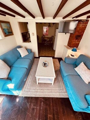 Una sala de estar con dos sofás azules, una mesa de centro blanca y un televisor fijado en una pared de ladrillo.
