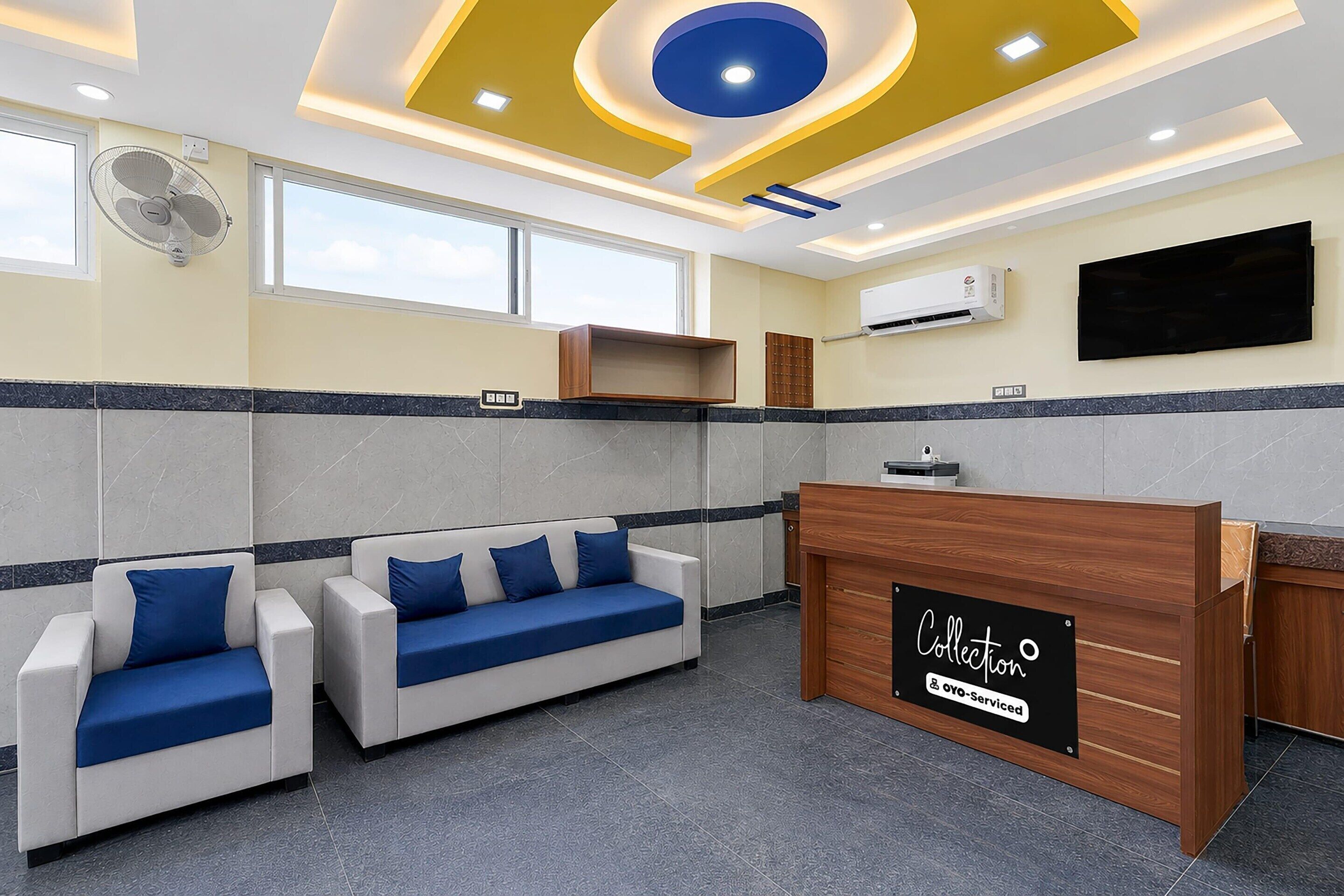 A hotel lobby with a reception desk, two sofas with blue cushions, a large window, and an air conditioning unit.